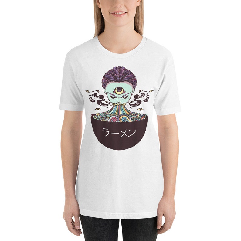 Peut inclure: T-shirt blanc avec un motif d'une cr&eacute;ature psych&eacute;d&eacute;lique color&eacute;e avec un troisi&egrave;me &oelig;il, mangeant des nouilles ramen dans un bol qui dit "ラーメン" en japonais.