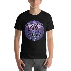May include: A black t-shirt with a graphic of a moth with a pink and purple gradient. The moth is surrounded by a circle with a geometric design and a single eye in the center.