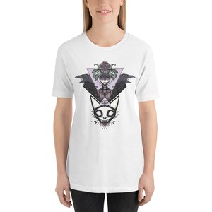 May include: White t-shirt with a graphic print of a woman with a floral crown and two ravens, a cat with an all-seeing eye, and a geometric triangle.
