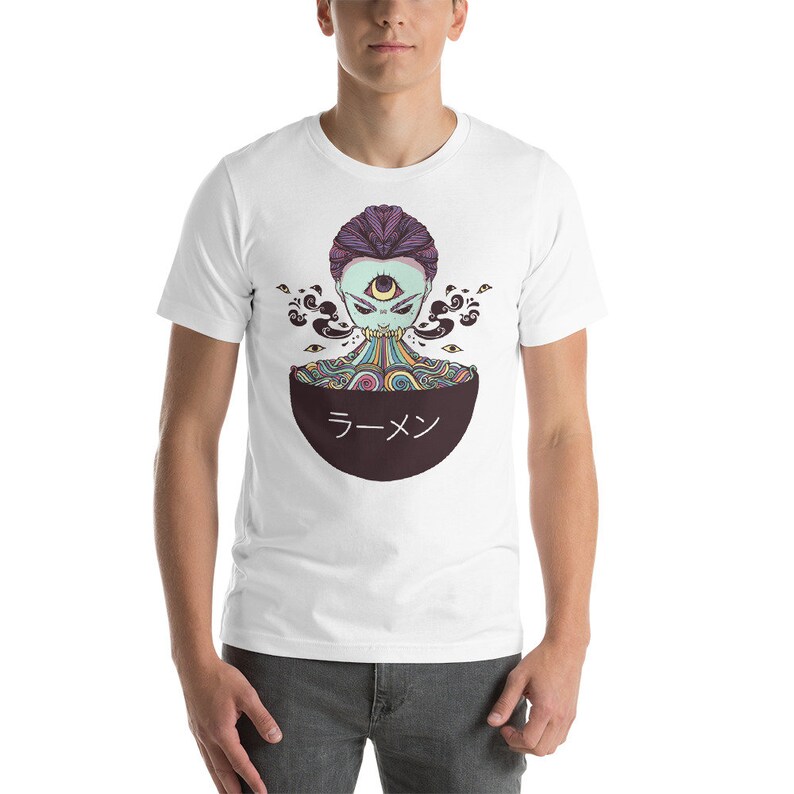 Peut inclure: T-shirt blanc avec un graphique d'une personne avec un troisi&egrave;me &oelig;il et des cheveux arc-en-ciel, mangeant des ramen dans un bol qui dit "Ramen" en japonais.