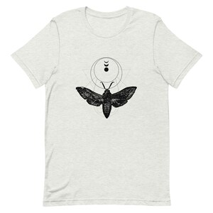 May include: A black and white graphic t-shirt featuring a moth with geometric shapes and crescent moons.