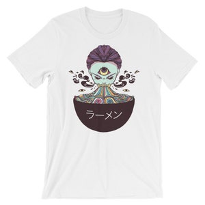 Peut inclure: T-shirt blanc avec un motif repr&eacute;sentant un personnage psych&eacute;d&eacute;lique color&eacute; avec un troisi&egrave;me &oelig;il, consommant un bol de ramen. Le bol est noir avec le mot "ラーメン" en blanc.