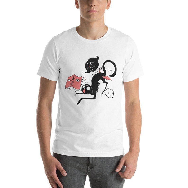 May include: White t-shirt with a black and white illustration of a cat, a ghost, and a book with eyes. The book is open and has the text "DREAMS" on the cover.
