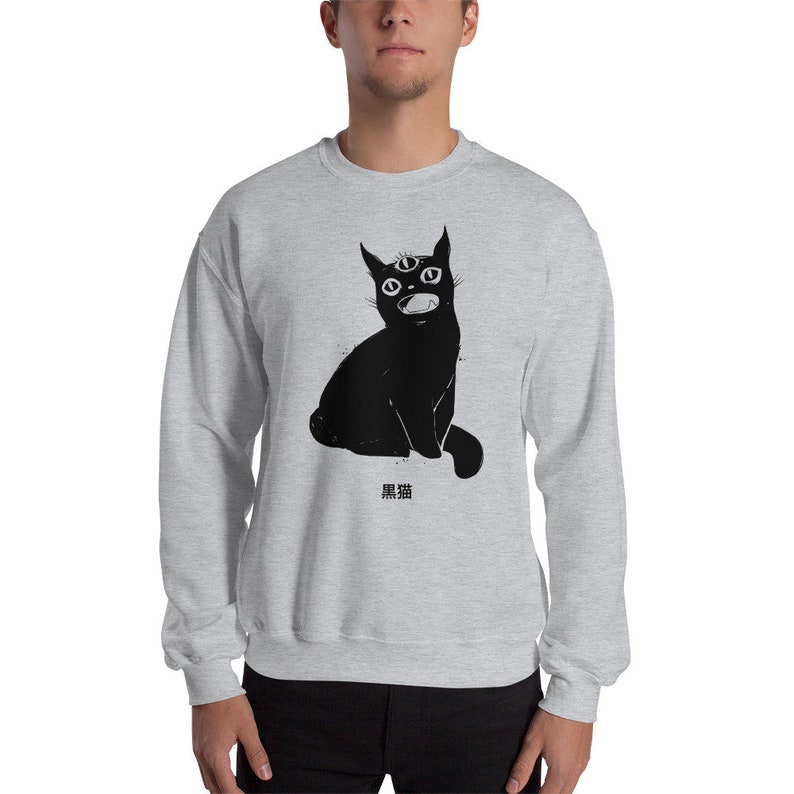 May include: A grey sweatshirt with a black cat illustration. The cat has three eyes and is sitting with its mouth open. The Japanese text "黒猫" is printed below the cat.