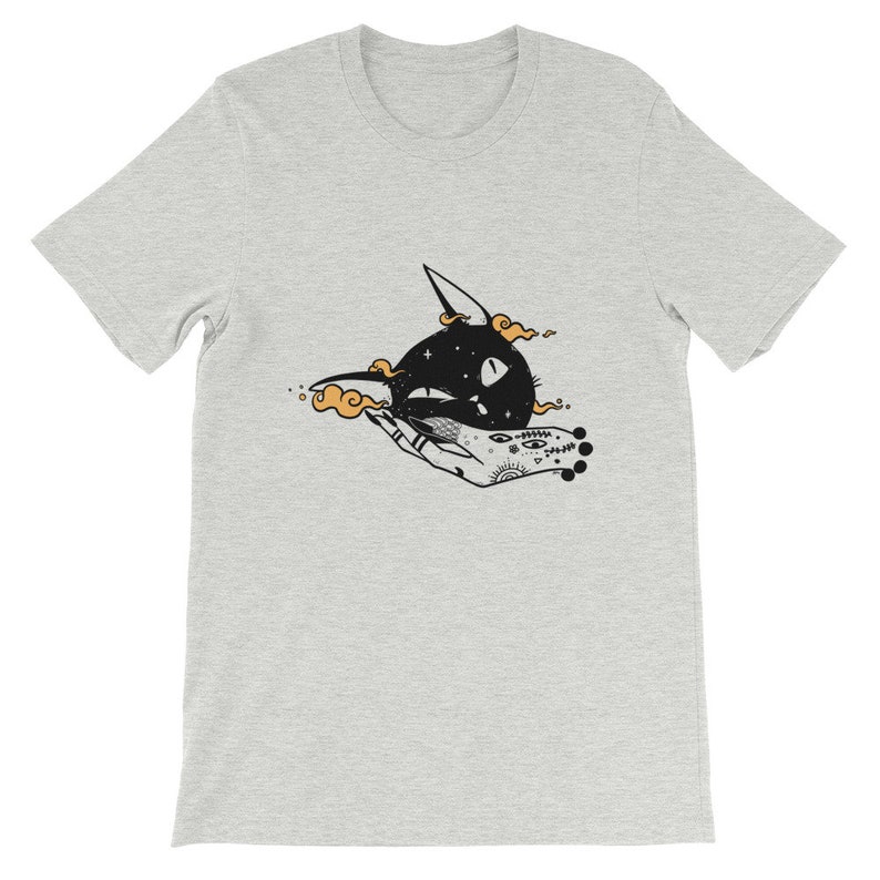 May include: A grey t-shirt with a black and white illustration of a cat's head with stars and a hand with a tattoo.