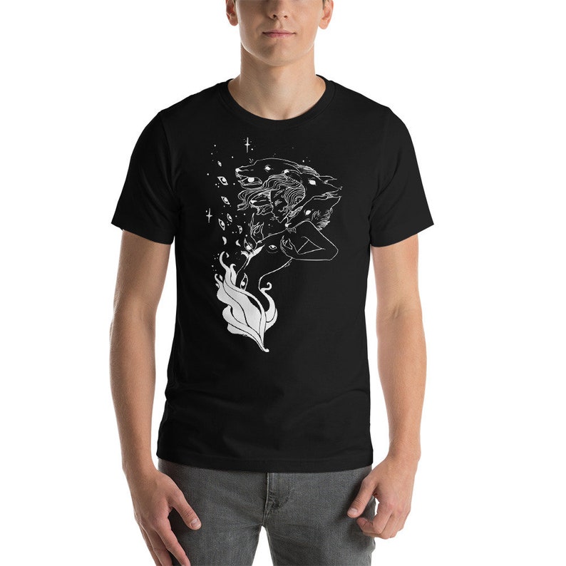 Op de afbeelding: Zwart T-shirt met een wit grafisch ontwerp van een vrouw met meerdere gezichten en ogen, omringd door een draaiend patroon van sterren en bladeren.