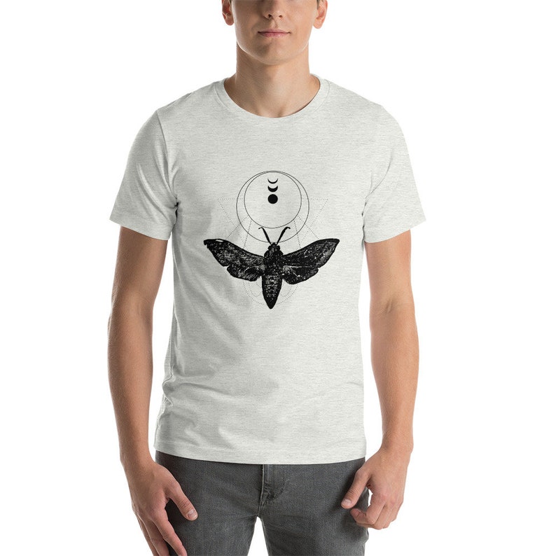 May include: A heather grey t-shirt with a black and white graphic of a moth with geometric shapes and crescent moons.