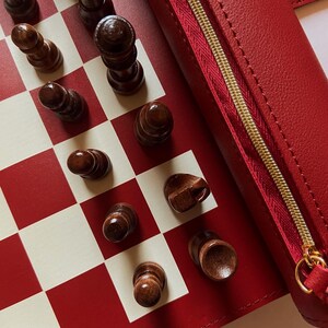 May include: A red and white checkered chess board with wooden chess pieces. A red leather case with a gold zipper is visible. The chess pieces are dark brown and arranged on the board.