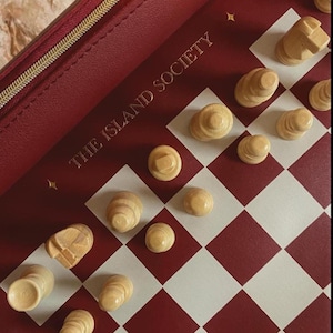 May include: A red and white checkered chess board with wooden chess pieces. The board is inside a red case with a gold zipper and the text "THE ISLAND SOCIETY".