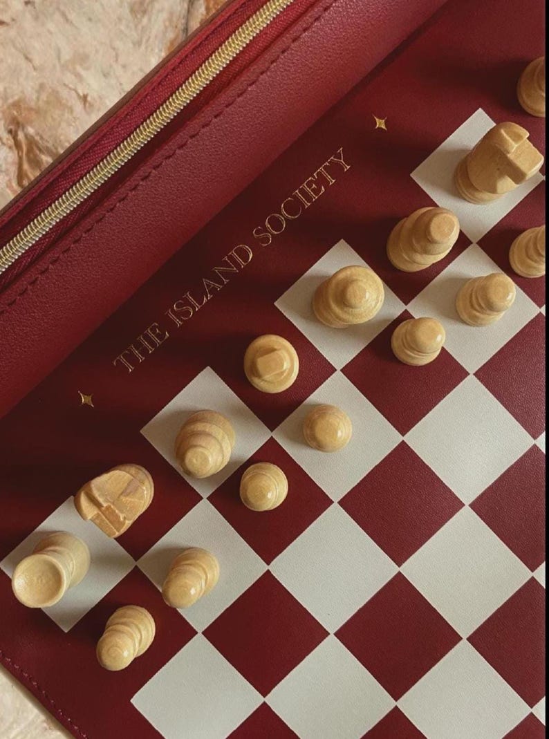 May include: A red and white checkered chess board with wooden chess pieces. The board is inside a red case with a gold zipper and the text "THE ISLAND SOCIETY".