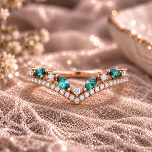 May include: A rose gold chevron ring featuring a row of small round white diamonds and four marquise-cut green gemstones. The band follows a V-shaped silhouette, with the green stones interspersed among the diamonds along the upper edge.
