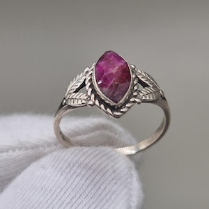Peut inclure: Une bague en argent ornée d'une pierre précieuse rose-rouge foncé de taille marquise, sertie dans une bordure en métal torsadé. L'anneau présente des motifs de feuilles détaillés de chaque côté de la pierre centrale.