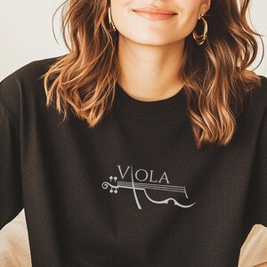 May include: Black t-shirt featuring the word "Viola" and a violin illustration in a light colour. The shirt is short-sleeved and casual.