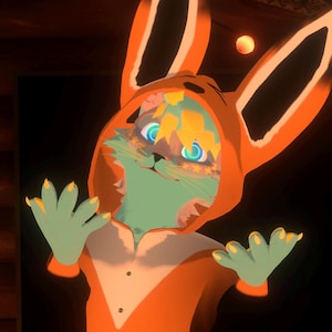 May include: A digital illustration of a creature wearing an orange fox-themed onesie. The creature has green skin, blue eyes, and yellow accents. The onesie has large ears and a hood. The creature is holding its hands up.