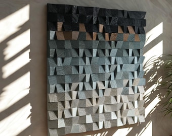 May include: A square, wooden wall art piece with a gradient design. The top portion is black, transitioning through shades of gray and brown to a light gray at the bottom. The artwork is made of small, textured wooden blocks.