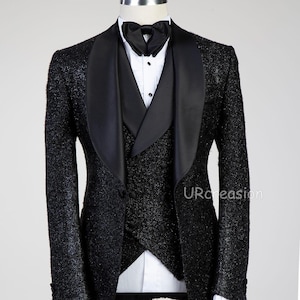 May include: A black tuxedo jacket and double-breasted vest with a shimmering, textured finish. The jacket features wide black satin shawl lapels. It is worn over a white dress shirt with a black bow tie. The text URcreasion is visible.