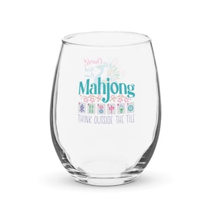 Puede incluir: Una copa de vino sin tallo transparente con la palabra "Mahjong" en color turquesa, con gráficos florales y de azulejos. El texto "THINK OUTSIDE THE TILE" está debajo. La copa está diseñada para jugar al juego de azulejos.