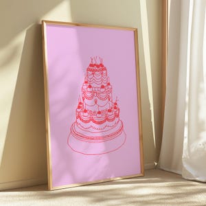 May include: A framed art print featuring a red line drawing of a tiered cake with cherries on a pink background. The cake has multiple layers with decorative frosting and is set against a light pink backdrop. The frame is a light brown color.