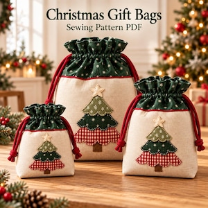 May include: Three drawstring gift bags in varying sizes made of beige fabric with a dark green top featuring a white snowflake pattern. Each bag displays a layered Christmas tree applique with a red gingham base and a star on top.
