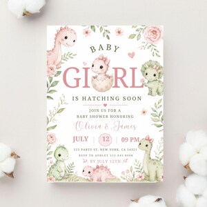 Puede incluir: Una invitación para baby shower con ilustraciones de dinosaurios y detalles florales. El texto dice "Baby Girl is Hatching Soon" con detalles para la fiesta de Olivia y James el 12 de julio a las 21:00.