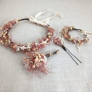 Peut inclure: Ensemble d'accessoires de cheveux floraux comprenant une couronne de fleurs, un petit serre-tête et un petit bouquet. Les fleurs sont roses et blanches, avec des tiges brunes et des détails en dentelle. Présenté sur une surface gris clair.
