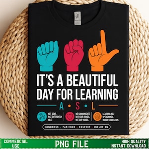 Może przedstawiać: Czarny t-shirt z trzema znakami dłoni w kolorze turkusowym, czerwonym i pomarańczowym, przedstawiającymi litery A, S i L. Napis głosi IT'S A BEAUTIFUL DAY FOR LEARNING ASL, wraz z ikonami i tekstem o komunikacji, życzliwości i integracji.