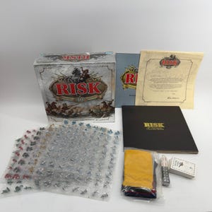 May include: The Risk 40th Anniversary Collector's Edition board game set includes a large illustrated box, a black game board folder, a certificate of authenticity, numerous plastic soldier figurines in sealed bags, a set of dice, and a deck of cards.