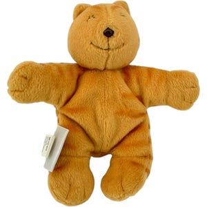 May include: A plush orange cat toy with brown stripes and a smiling face. The stuffed animal has outstretched arms and a small tag attached to its side. The toy is made of soft, fuzzy material.