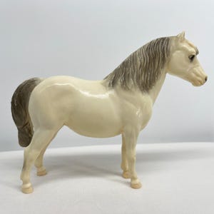 May include: A cream-colored horse figurine with a gray mane and tail. The horse is standing, showcasing its detailed features. This collectible item is a decorative piece, perfect for animal lovers and collectors.