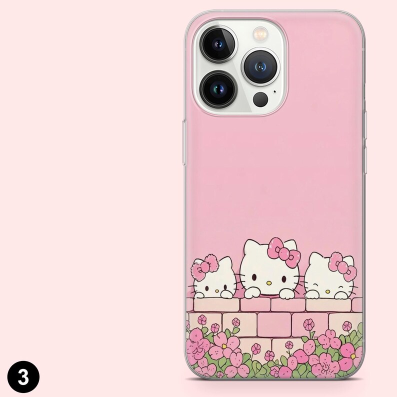 May include: Pink phone case featuring three Hello Kitty characters peeking over a brick wall with pink flowers. The case has a clear border and a pink background. The phone's camera lenses are visible.