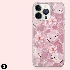May include: A clear phone case with a pink and white pattern of Hello Kitty faces and pink cherry blossoms. The case has a glossy finish and a clear border, showing the phone's camera.