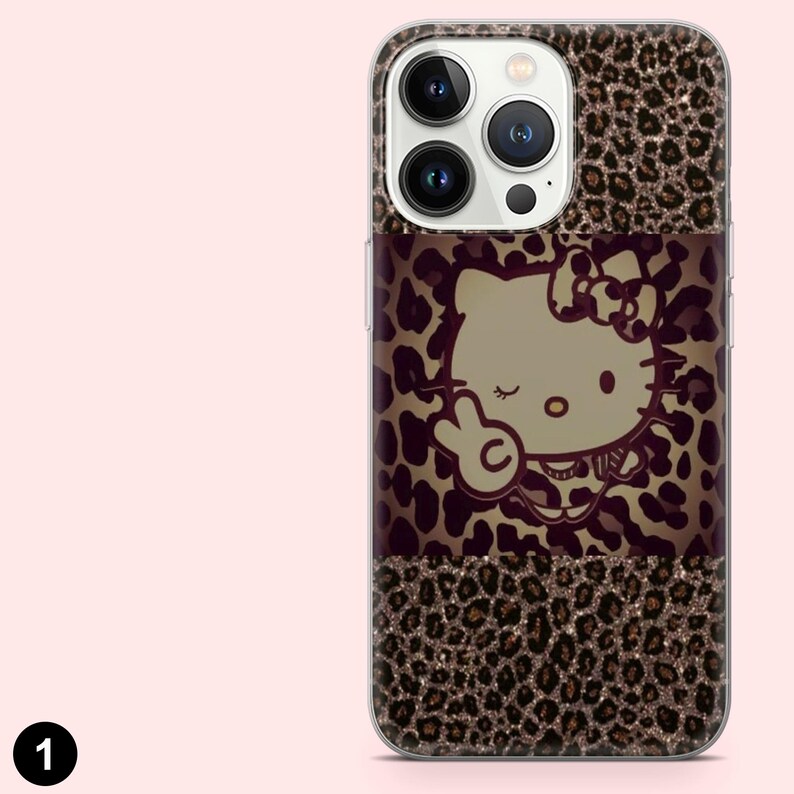 May include: A phone case with a leopard print design and a Hello Kitty graphic. The case has a clear border and a brown, black, and gold color scheme. The Hello Kitty graphic is in the center of the case.