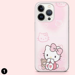 May include: A clear phone case with a pink background featuring a Hello Kitty design. The design includes multiple Hello Kitty illustrations, hearts, and a large Hello Kitty character with a bow and a teddy bear.