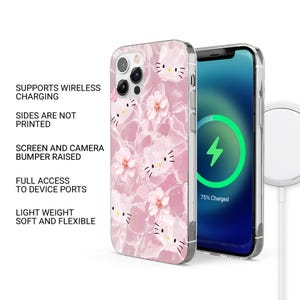 May include: A pink phone case with a repeating pattern of a cartoon cat face and flowers. The phone case is on a phone with a charging symbol on the screen. The case supports wireless charging and has full access to device ports.