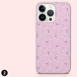 以下が含まれることがあります： ピンク色の携帯電話ケース。白いハローキティの顔、花、ハート、蝶の繰り返し模様。ケースは透明で光沢のある仕上がりで、スマートフォン向けに設計されています。