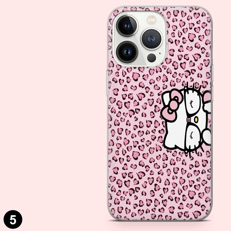 May include: A pink phone case with a leopard print pattern of pink hearts. The case features a white cartoon character with a pink bow and glasses. The phone case has a camera and flash.