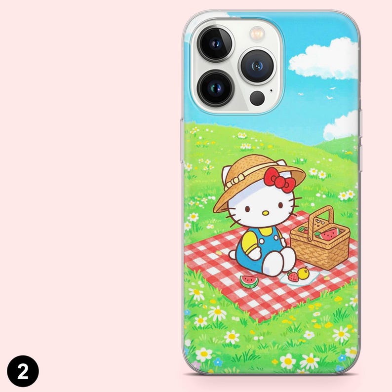May include: Clear phone case featuring a cartoon illustration of Hello Kitty having a picnic. The design includes a red and white checkered blanket, a picnic basket, and a sunny outdoor scene with blue skies and green grass.