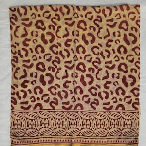 Può includere: Sciarpa beige con un motivo leopardato bordeaux ripetuto. Il bordo inferiore presenta un motivo decorativo con una sottile striscia verde, gialla e rossa. La sciarpa è realizzata in tessuto leggero.