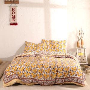 Könnte beinhalten: Ein Bettwäsche-Set mit floralem Muster mit weißem Hintergrund, gelben Blumen und braunen Stielen. Das Set enthält einen Bettbezug und zwei Kissenbezüge. Der Rand hat ein braunes und gelbes Design. Ein Wandbehang mit dem Wort "HOME" ist sichtbar.