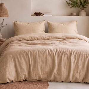 May include: A beige linen duvet cover set featuring a textured fabric finish. The bedding includes a large duvet cover draped over a bed and two matching rectangular pillowcases, all in a solid, neutral light tan color with visible fabric weave.