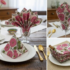 May include: Cloth napkins with a pink floral pattern on a cream background are displayed in different ways. Gold cutlery and white plates are set on a wooden table, creating a dining scene. Napkins are folded in various styles.