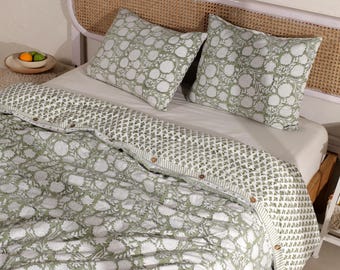 May include: A bed set featuring a green and white floral pattern. The set includes a comforter and two matching pillowcases. The comforter has a geometric border and wooden button closures. The headboard is made of woven rattan.