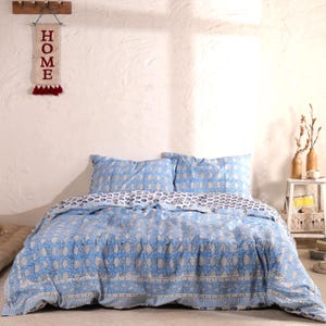 May include: A white ceramic mug with a black handle and the text "But First, Coffee" in a bold, black font. The mug is set against a blurred background, suggesting a cozy setting.