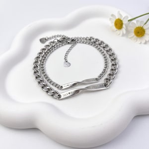 May include: Two silver-toned metal chain bracelets featuring a central twisted bar element. One bar is engraved with 'Ava heart Jack' and '2022.4.8', while the other displays 'Jack heart Ava' and '2022.4.8'. Each bracelet includes a small heart charm.
