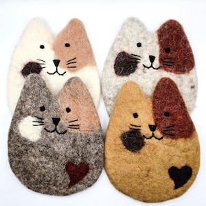 Peut inclure: Quatre dessous de verre en laine feutrée en forme de chat. Chaque dessous de verre présente un motif de couleur unique, avec des taches blanches, fauves, grises et brunes. Chaque visage de chat a des yeux, un nez et des moustaches noirs brodés.