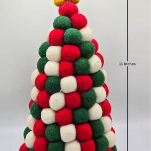 May include: A conical Christmas tree decoration constructed from numerous red, green, and white felt balls, topped with a yellow felt star. The tree measures 11 inches in height and 6 inches in width as indicated by the visible measurement lines.