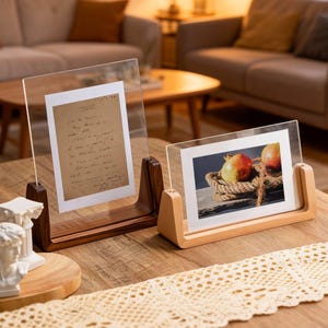 Puede incluir: Dos marcos de fotos de acrílico transparente con bases de madera. Uno contiene un documento manuscrito, el otro muestra una foto de granadas en una cesta. Los marcos están sobre una mesa de madera.