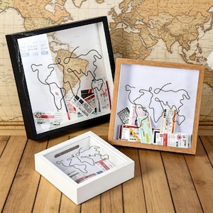 May include: Three shadow box frames in black, white, and natural wood. Each frame features a wire outline of a world map and holds travel tickets. The frames are displayed on a wooden surface with a vintage world map in the background.