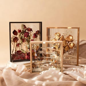 Puede incluir: Tres cajas decorativas con flores secas. Las cajas tienen marcos negros, dorados y de madera natural. Las flores son en tonos rojos, dorados y blancos. El texto en la caja del medio dice "Jesus Christ, The Way to Eternity."
