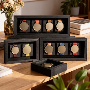 Puede incluir: Varias cajas de exhibición de madera negra con medallas de oro y cintas de colores. Las cajas están dispuestas sobre una superficie de madera, mostrando las medallas. Algunas cajas contienen múltiples medallas, otras una sola.